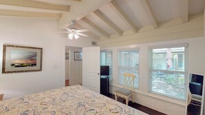 A bedroom with a bed, a ceiling fan, a window with blinds, and a door leading to another room.