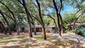 A house surrounded by trees with a red door and a small porch with two chairs.