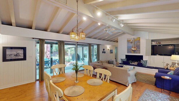 A spacious living area with a high ceiling, a fireplace, a television, and a dining area with a wooden table and chairs.