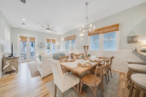 A spacious dining area with a wooden table set for six, surrounded by wicker chairs, and a ceiling fan above.
