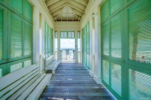 A covered wooden walkway with benches, flanked by green shutters, leading to a view.