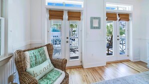 Una habitación con una silla de mimbre, una puerta con vistas y piso de madera.