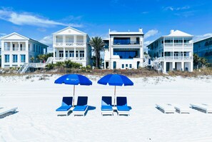 A beachfront property with multiple-story buildings, a sandy beach with lounge chairs, and umbrellas.