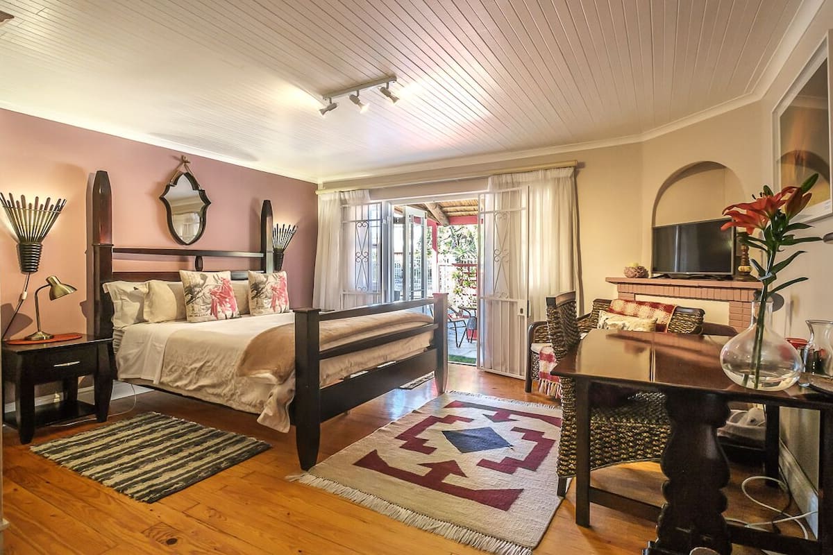 A bedroom with a bed, bedside table, lamp, and a view of the outside.
