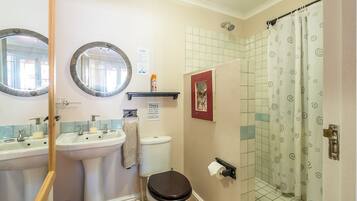 A bathroom with two sinks, a toilet, a shower with a patterned curtain, and a mirror.