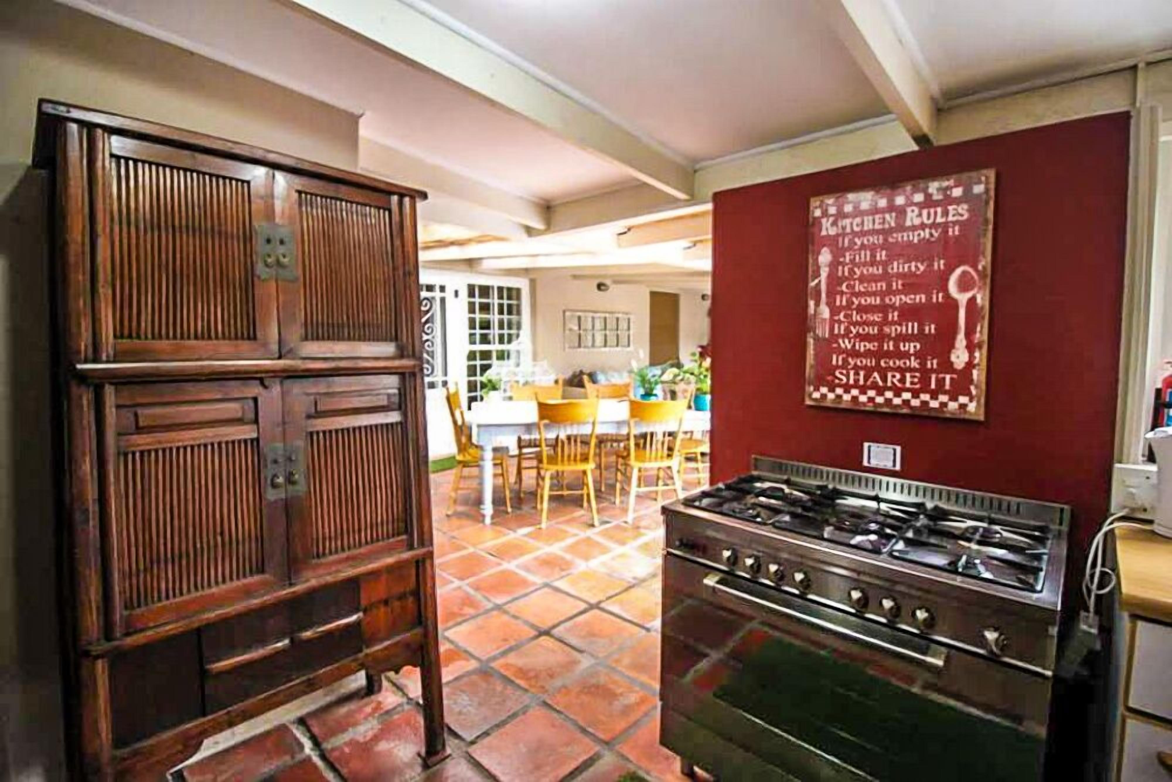 Una cocina con estufa a gas, armarios de madera y suelo de baldosas. Hay un cartel con normas de la cocina en la pared.