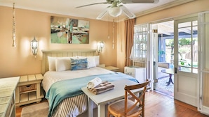 A bedroom with a bed, a table, a chair, a ceiling fan, and a view of the outdoors. - Inn Style Guesthouse (Cape Town)