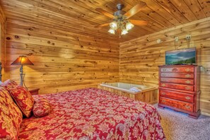 Ein Schlafzimmer in einer Holzhütte mit einem Bett, einer Holzkammer, einem Deckenventilator und einem Fernseher.