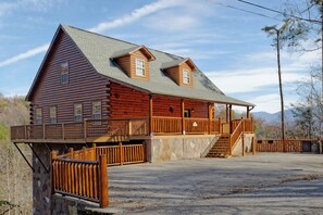 Une cabane en rondins avec des fondations en pierre, un balcon et un escalier menant à l’entrée principale.