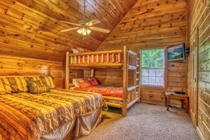 Een slaapkamer in een houten chalet met een stapelbed, een enkel bed, een plafondventilator en een raam met zonwering.