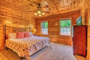 Ein Schlafzimmer einer Holzhütte mit einem Bett, zwei Fenstern, einem Deckenventilator und einer Kommode.