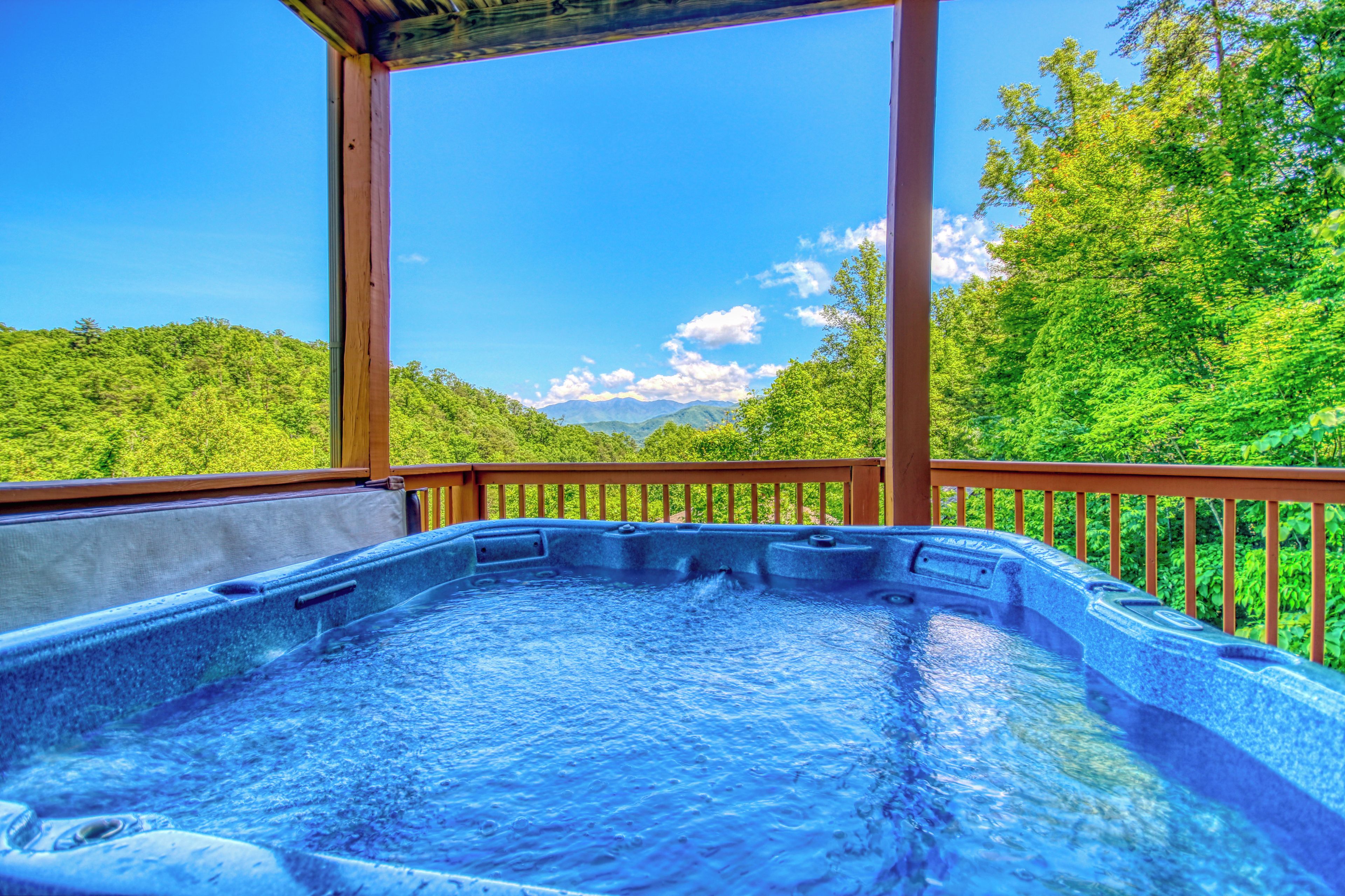 A hot tub with a wooden deck and a view of a forested mountain range.