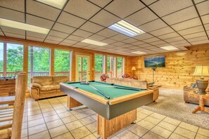 Une table de billard dans une pièce aux murs en bois et aux grandes fenêtres.