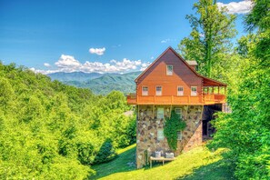 Een vakantiehuis in blokhutstijl met een stenen fundering, een balkon en uitzicht op bergen.