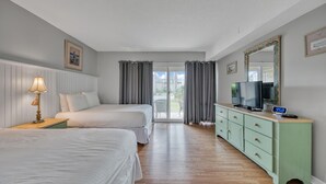 Habitación de hotel con dos camas, televisor, cómoda y puerta corrediza al exterior.