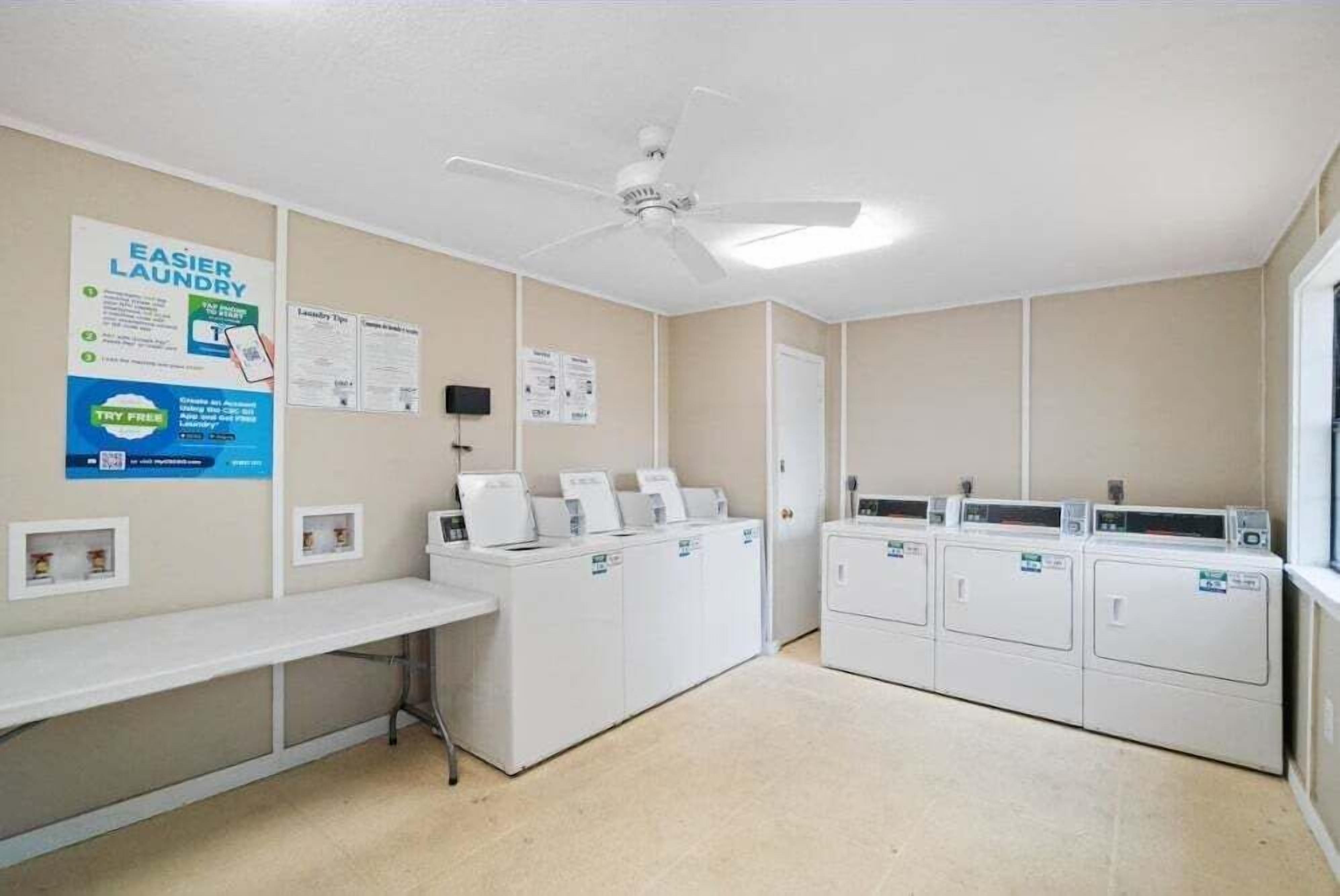 A laundry room with multiple washing machines, a drying rack, and informational posters on the walls.
