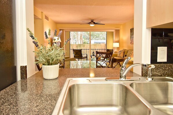 A kitchen with stainless steel sinks, a potted plant, and a dining area with chairs and a table.
