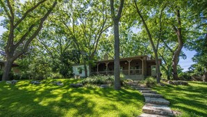 Une maison avec un chemin de pierre menant à un porche, entourée d’une végétation luxuriante et d’arbres.