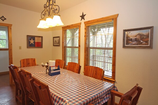 A dining room with a checkered tablecloth, wooden chairs, a chandelier, and a Texas flag.