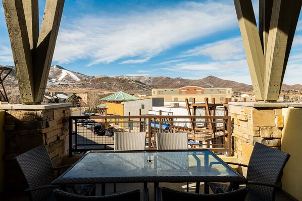 Un balcon avec une table et des chaises, donnant sur un paysage montagneux avec des bâtiments en arrière-plan.