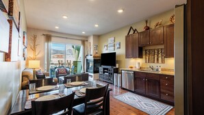 A dining area with a table set for four, a television, and a kitchen with wooden cabinets and a refrigerator. - Bright and Airy Mountain Townhome. Walk to Shops, Dining, Trails + Hot Tub (Park City)