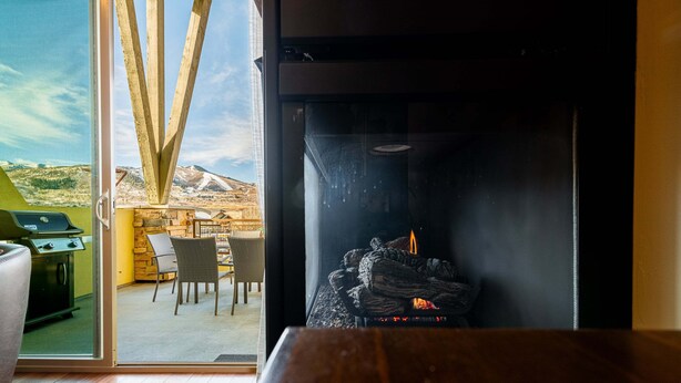 A room with a fireplace, a dining area with chairs, and a view of a mountainous landscape through large glass doors. - Bright and Airy Mountain Townhome. Walk to Shops, Dining, Trails + Hot Tub (Park City)