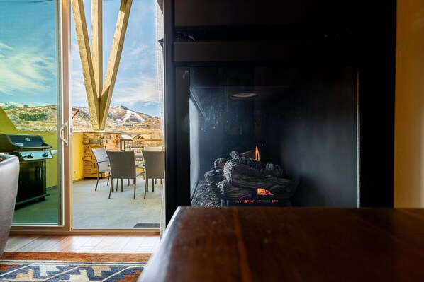 A room with a fireplace, a dining area with chairs, and a view of a mountainous landscape through large glass doors. - Bright and Airy Mountain Townhome. Walk to Shops, Dining, Trails + Hot Tub (Park City)
