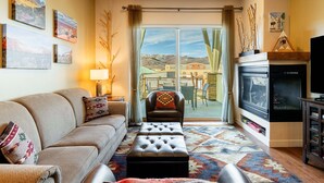A living room with a sofa, ottoman, fireplace, television, and artwork on the walls. - Bright and Airy Mountain Townhome. Walk to Shops, Dining, Trails + Hot Tub (Park City)