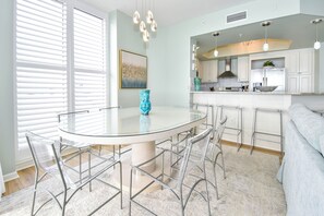 A modern kitchen with white cabinets, a central island with a glass top, and bar stools. - Cool, Tropical Beachfront Condo w/ Great Views in Central Destin! 🌅🌺🐬 (Destin)