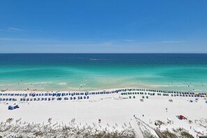 A beach with rows of umbrellas and beach chairs, a sandy shore, and the ocean. - Cool, Tropical Beachfront Condo w/ Great Views in Central Destin! 🌅🌺🐬 (Destin)