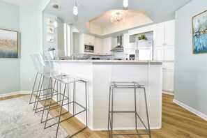 A modern kitchen with white cabinets, stainless steel appliances, and a central island with bar stools. - Cool, Tropical Beachfront Condo w/ Great Views in Central Destin! 🌅🌺🐬 (Destin)
