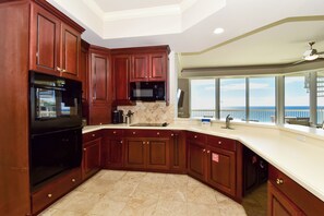 A kitchen with dark wooden cabinets, a black microwave, and a large window offering a view of the ocean.