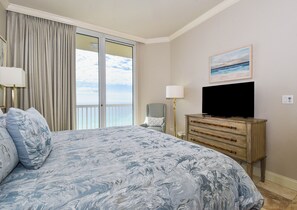 A hotel room with a large bed, a television on a wooden dresser, a chair, and a view of the ocean through a sliding door. - Spacious beachfront penthouse w/private rooftop terrace in Destin! 🐚🌴🌊 (Destin)