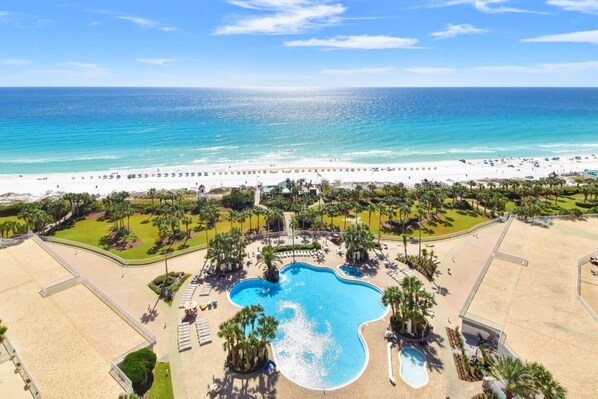 A resort with a large pool, beach access, and palm trees.