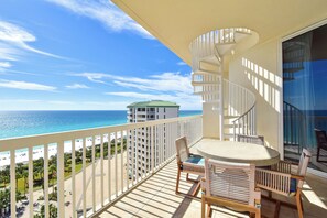 A balcony with a round table and chairs, overlooking a beach and ocean.