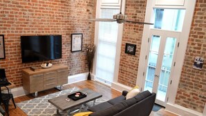 Un salon avec un mur en briques, un téléviseur à écran plat, une table basse en bois, un canapé et une porte avec des panneaux de verre.