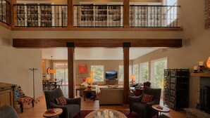 A spacious living area with a high ceiling, a fireplace, and a balcony with bookshelves. - Spacious 7BR Lakeside Ski Lodge, Hot Tub, Game Room (Durango)