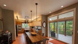 A spacious kitchen with a large dining table, a built-in oven, and a view of the outdoors through a sliding glass door. - Spacious 7BR Lakeside Ski Lodge, Hot Tub, Game Room (Durango)