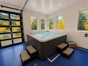 A hot tub with four steps, a window with a view of yellow foliage, and a basket of towels. - Spacious 7BR Lakeside Ski Lodge, Hot Tub, Game Room (Durango)