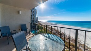 Ein Balkon mit Glastisch und Stühlen mit Blick auf einen Strand.