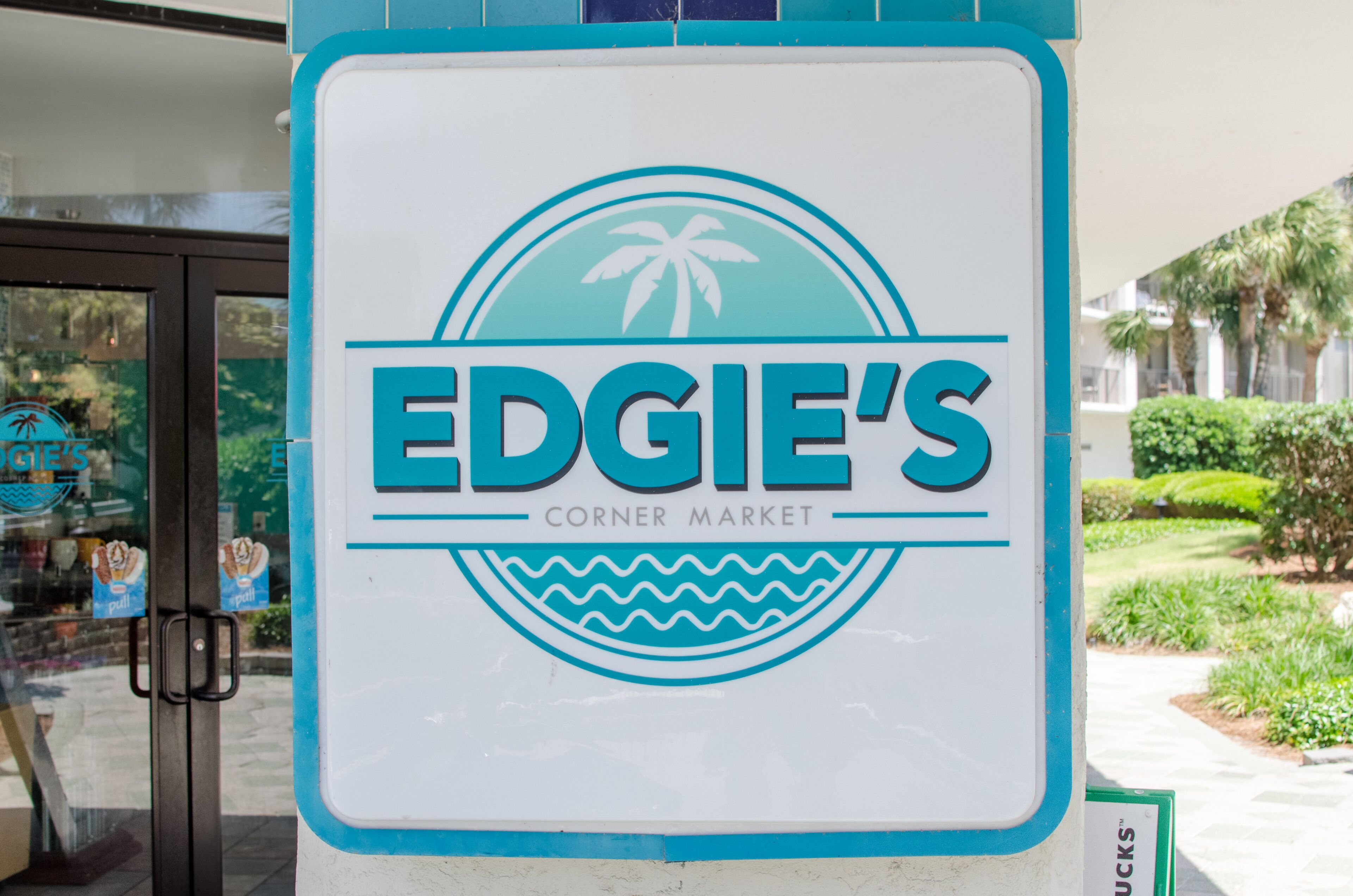 Placa para Edgie's Corner Market com ilustração de palmeira e ondas.