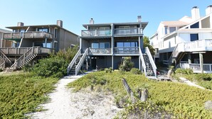 Een strandhuis met meerdere verdiepingen, balkons en een trap naar de bovenverdiepingen.