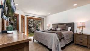 A bedroom with a bed, bedside tables, a desk, a TV, and a view of the outdoors.