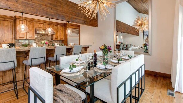A modern kitchen with wooden cabinetry, a glass dining table, and pendant lighting.
