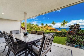 A dining area with a table and chairs, a view of a tropical landscape with palm trees and a building in the distance.