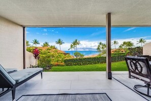 A sunlit patio with a view of the ocean and palm trees.