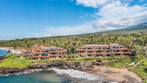 A coastal resort with multiple buildings, a beach, and a mountainous backdrop. - Experience luxury at Makena Surf #C-102, a spacious 2-bedroom condo with ocean views in Makena. (Makena, Maui)