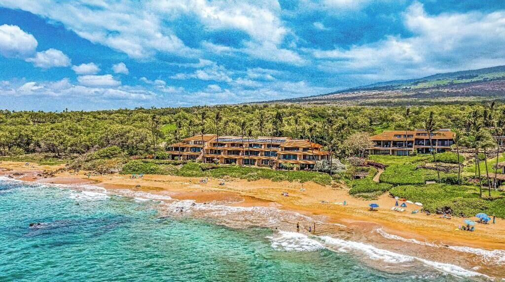 Un hôtel situé en bord de mer, composé de plusieurs bâtiments, avec une plage de sable fin et une eau turquoise cristalline.