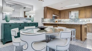 A modern kitchen with a central island, white chairs, and a teal cabinet.