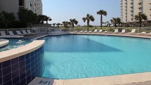 Piscina com profundidade de 1,10 metros, rodeada por espreguiçadeiras e palmeiras, com um edifício alto ao fundo.